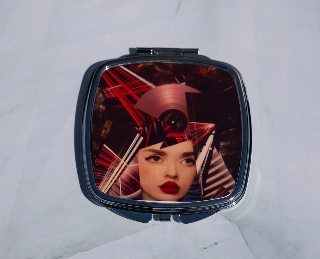Square personalised compact mirror with abstract mixed media portrait artwork on a metal case, displayed open on a marble background.