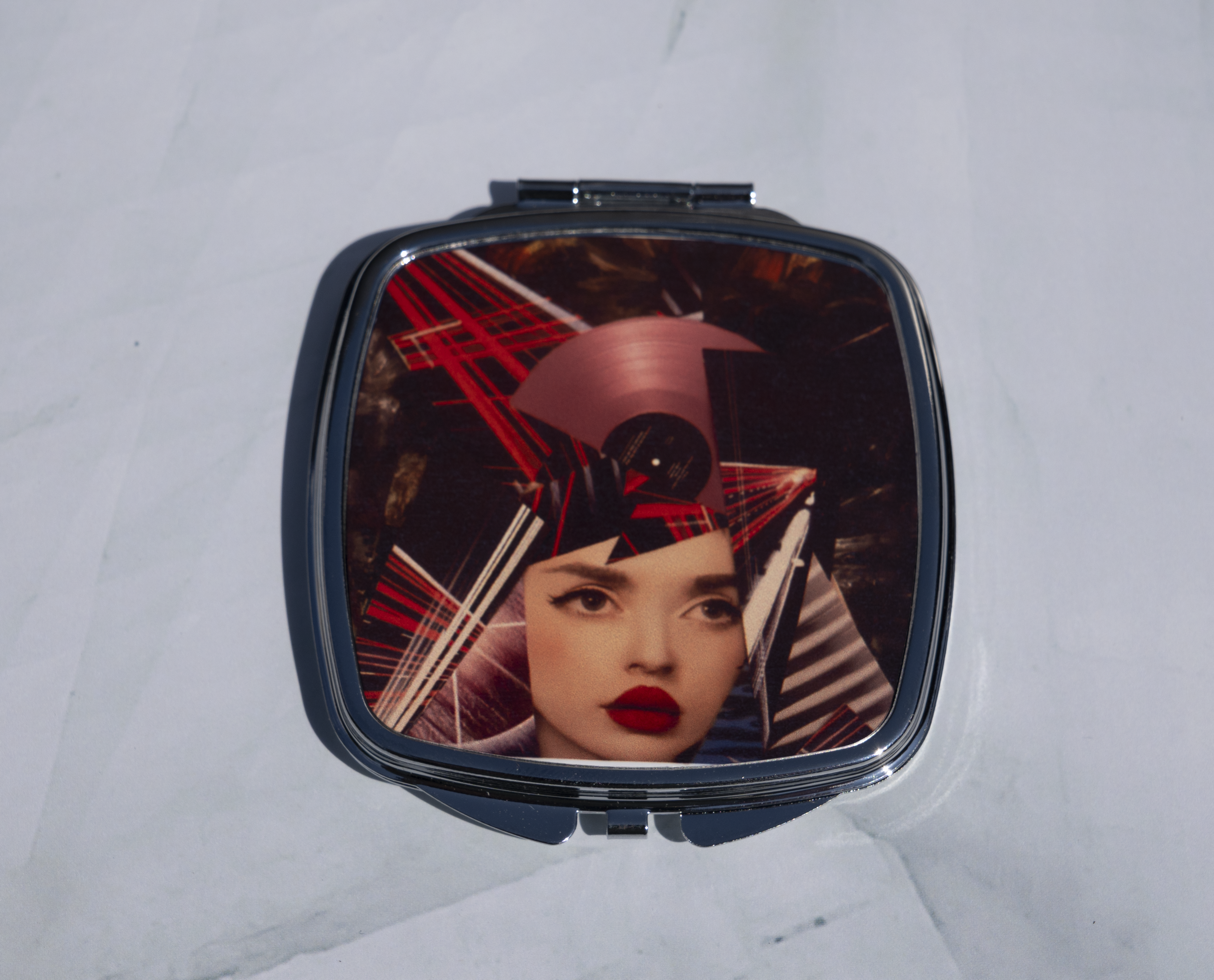 Square personalised compact mirror with abstract mixed media portrait artwork on a metal case, displayed open on a marble background.